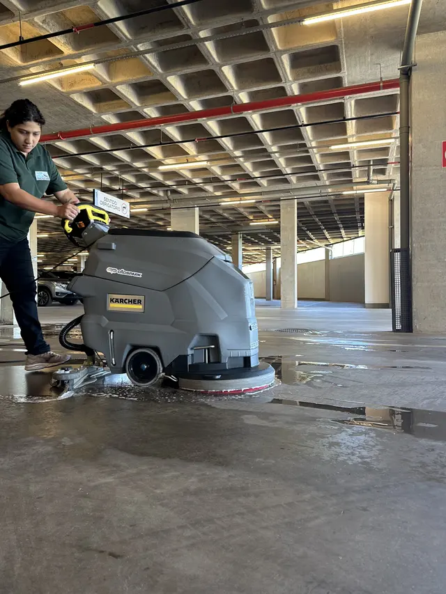 Colaboradora operando máquina de limpeza de piso na garagem